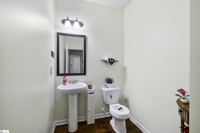 half bath featuring a sink, toilet, wood finished floors, and baseboards