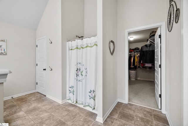 bathroom featuring curtained shower, baseboards, a spacious closet, and lofted ceiling