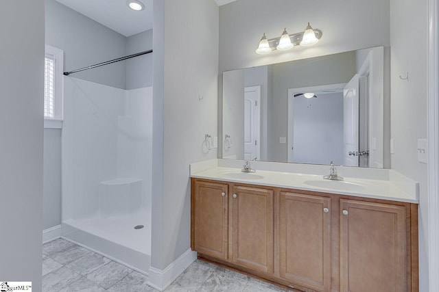 full bathroom with double vanity, walk in shower, baseboards, and a sink