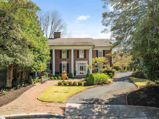 neoclassical / greek revival house featuring brick siding, driveway, and a chimney