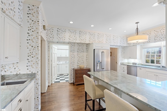 kitchen featuring wallpapered walls, ornamental molding, light stone countertops, stainless steel appliances, and a sink