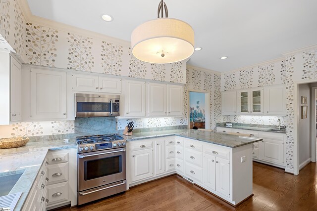 kitchen with stainless steel appliances, white cabinetry, wallpapered walls, and ornamental molding