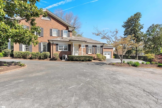 view of front of house with a garage, aphalt driveway, brick siding, and fence