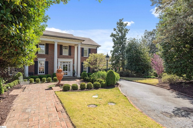 greek revival inspired property with french doors, a front yard, and brick siding