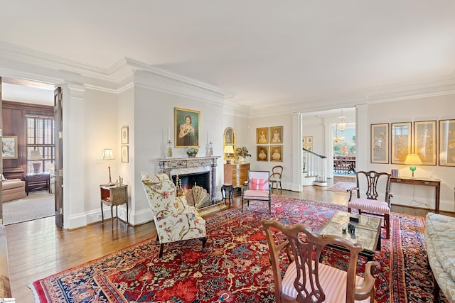 living area with crown molding, wood-type flooring, ornate columns, and a premium fireplace