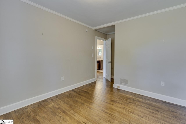 empty room featuring wood finished floors, baseboards, ornamental molding, and visible vents