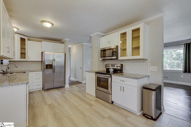 kitchen with glass insert cabinets, light stone countertops, white cabinetry, appliances with stainless steel finishes, and a sink