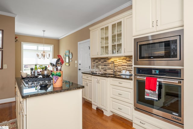 kitchen featuring crown molding, light wood-type flooring, a sink, stainless steel appliances, and decorative backsplash