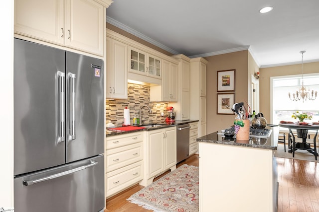 kitchen with cream cabinets, crown molding, light wood-style floors, appliances with stainless steel finishes, and a sink