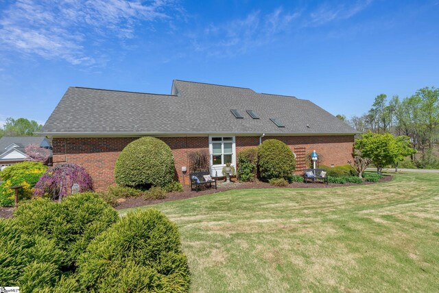 rear view of property with roof with shingles, a yard, and brick siding