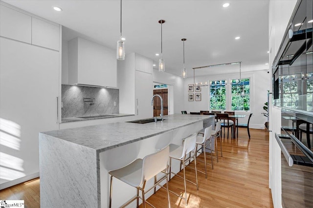 kitchen featuring modern cabinets, a kitchen bar, white cabinetry, light wood finished floors, and decorative backsplash