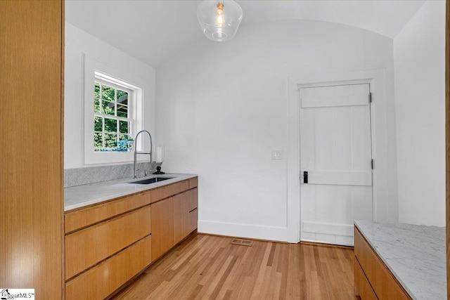bar featuring visible vents, baseboards, a sink, light wood finished floors, and lofted ceiling