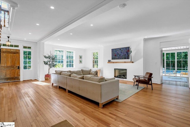 living area featuring a glass covered fireplace, baseboards, recessed lighting, crown molding, and light wood finished floors