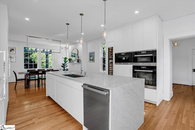 kitchen with an island with sink, white cabinets, modern cabinets, light wood finished floors, and a sink