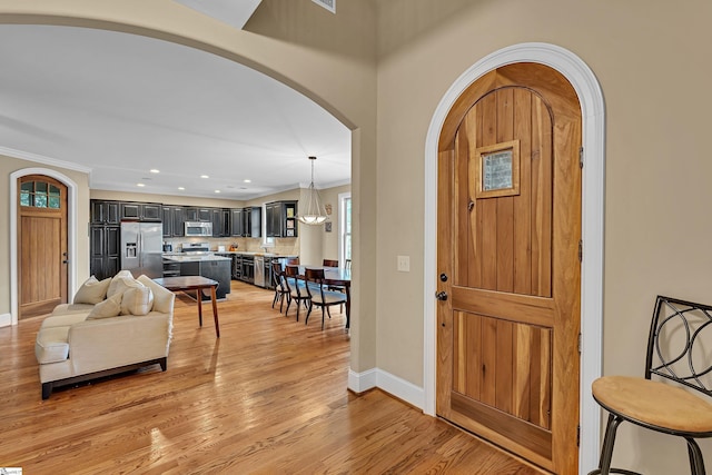 entrance foyer featuring baseboards, arched walkways, light wood-style floors, crown molding, and recessed lighting