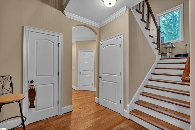 stairway with arched walkways, wood finished floors, crown molding, and baseboards