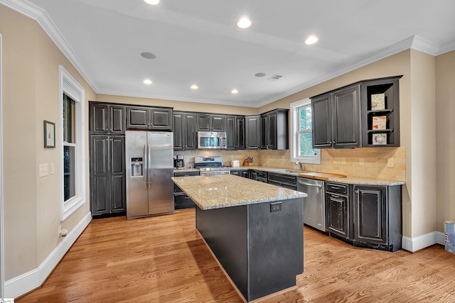 kitchen featuring a sink, ornamental molding, stainless steel appliances, light wood-style flooring, and a kitchen island