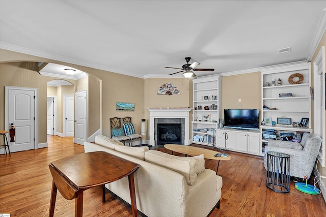 living room featuring visible vents, arched walkways, a ceiling fan, light wood-style flooring, and a glass covered fireplace