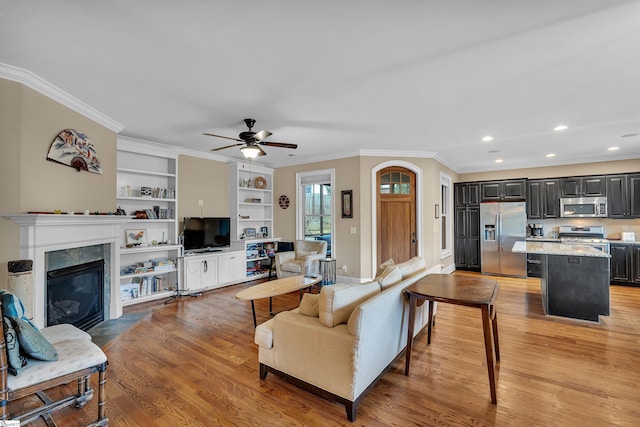 living room featuring a fireplace, light wood finished floors, a ceiling fan, and ornamental molding
