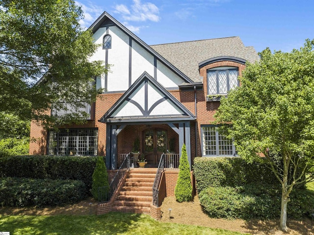 view of front of property with roof with shingles, brick siding, french doors, and stucco siding
