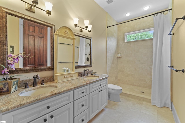 full bathroom featuring a tile shower, double vanity, a sink, and toilet