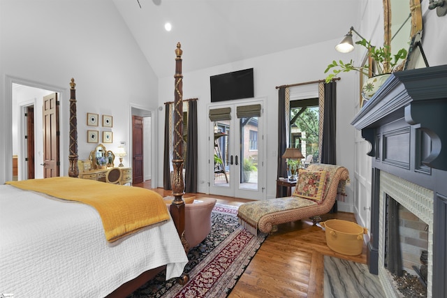 bedroom with wood finished floors, a fireplace with flush hearth, french doors, access to exterior, and high vaulted ceiling