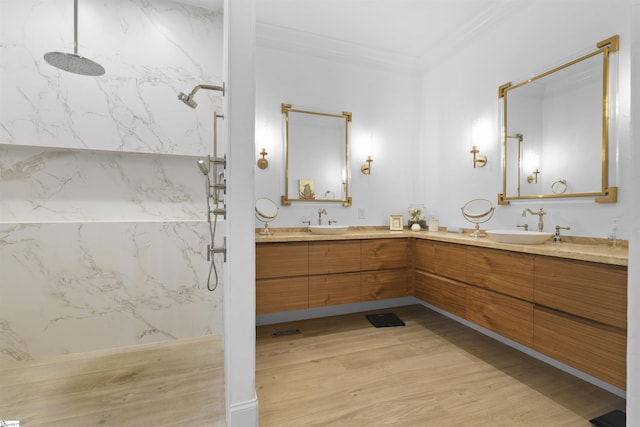 bathroom with ornamental molding, wood finished floors, a sink, a marble finish shower, and double vanity