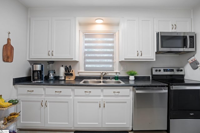 kitchen with appliances with stainless steel finishes, a sink, white cabinetry, and dark countertops