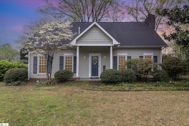 view of front of home with a chimney, a shingled roof, and a lawn