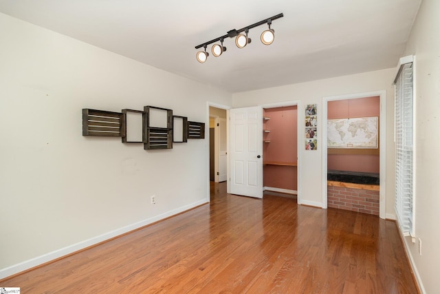 empty room with rail lighting, baseboards, and wood finished floors