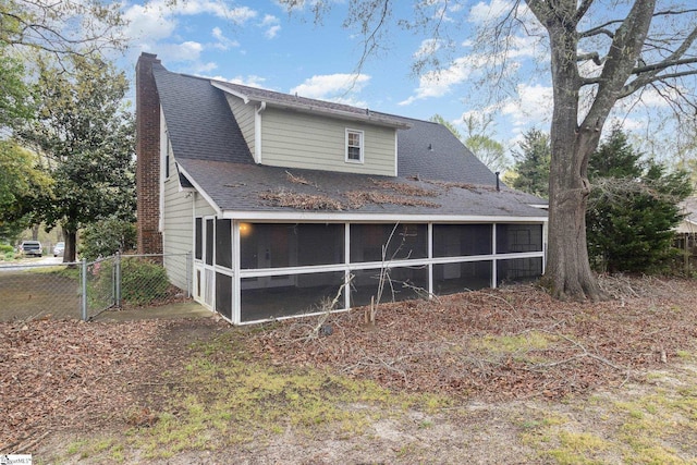 rear view of property with a sunroom, a chimney, a shingled roof, and fence