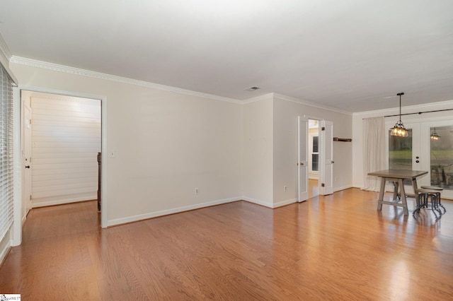 unfurnished living room featuring a notable chandelier, light wood-style floors, baseboards, and crown molding
