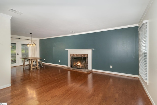 unfurnished living room with a brick fireplace, visible vents, ornamental molding, and wood finished floors