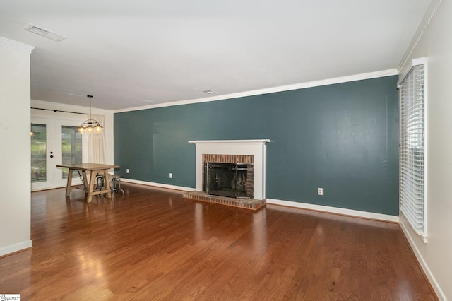 unfurnished living room with crown molding, visible vents, a brick fireplace, and wood finished floors