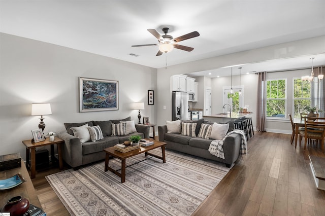 living area with visible vents, ceiling fan with notable chandelier, baseboards, and wood finished floors
