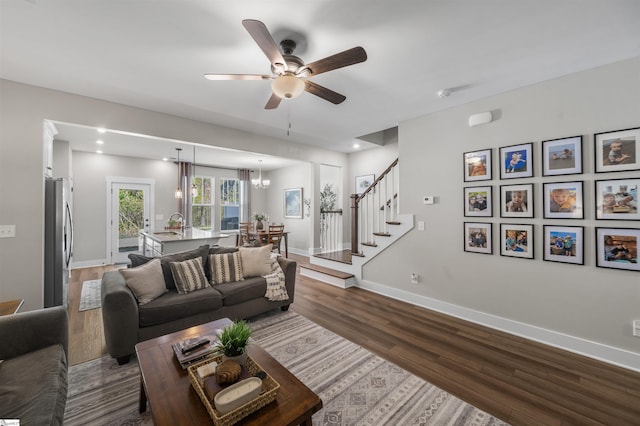living room featuring baseboards, dark wood-style flooring, stairway, recessed lighting, and ceiling fan with notable chandelier
