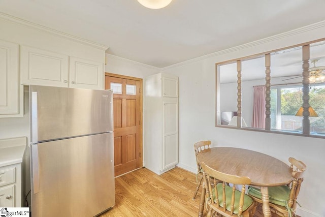 kitchen featuring white cabinets, light countertops, freestanding refrigerator, crown molding, and light wood finished floors