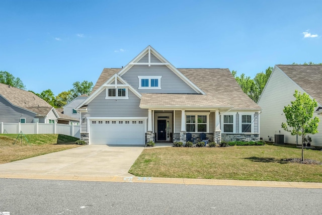 craftsman-style house with central air condition unit, covered porch, fence, a front lawn, and driveway