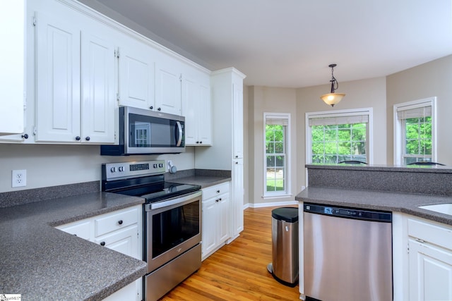 kitchen with dark countertops, white cabinets, light wood-style floors, appliances with stainless steel finishes, and hanging light fixtures