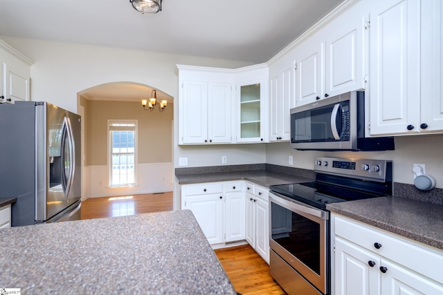 kitchen featuring arched walkways, an inviting chandelier, dark countertops, light wood-type flooring, and appliances with stainless steel finishes