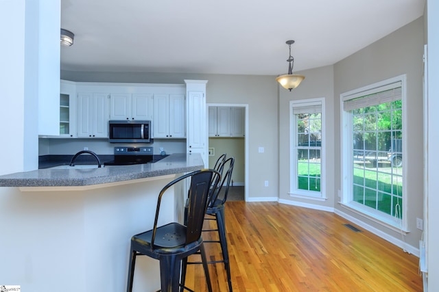 kitchen with visible vents, white cabinets, light wood-type flooring, a kitchen bar, and stainless steel appliances
