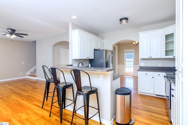 kitchen featuring ceiling fan, arched walkways, white cabinets, stainless steel appliances, and a breakfast bar area
