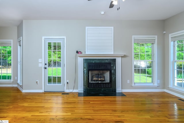 unfurnished living room with baseboards, a ceiling fan, wood finished floors, and a high end fireplace