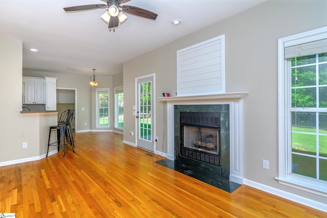 unfurnished living room with light wood-type flooring, ceiling fan, a fireplace, and baseboards