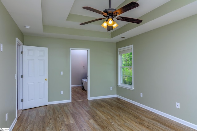 unfurnished bedroom featuring visible vents, a tray ceiling, baseboards, and wood finished floors