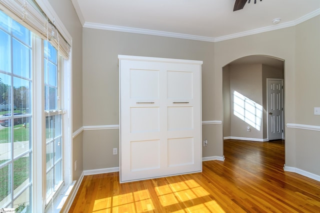 spare room featuring baseboards, arched walkways, plenty of natural light, and light wood-style floors
