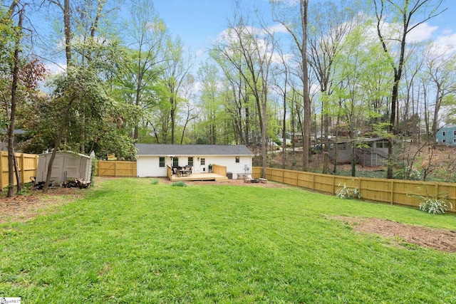 view of yard with a shed, an outbuilding, a fenced backyard, and a deck
