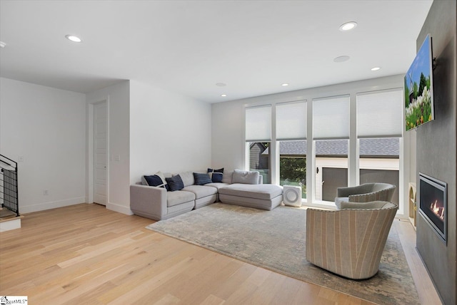 living area featuring light wood-type flooring, baseboards, a large fireplace, and recessed lighting