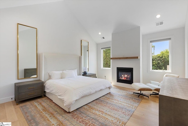 bedroom featuring visible vents, recessed lighting, wood finished floors, a glass covered fireplace, and lofted ceiling