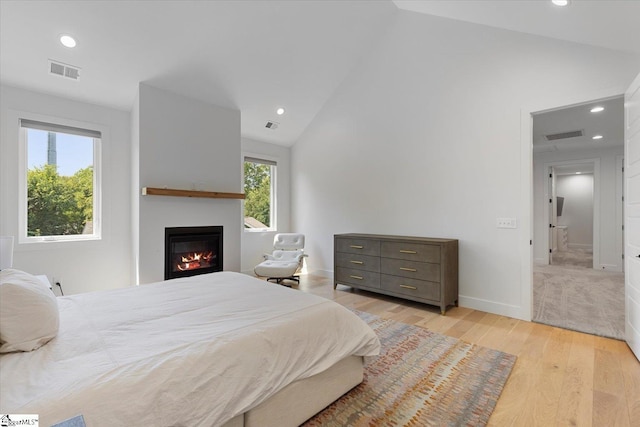 bedroom with a glass covered fireplace, recessed lighting, light wood-style floors, and visible vents